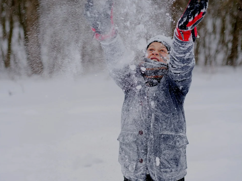 Enfant qui lance de la neige dans les airs et dont l'habit est recouvert de neige (hiver)